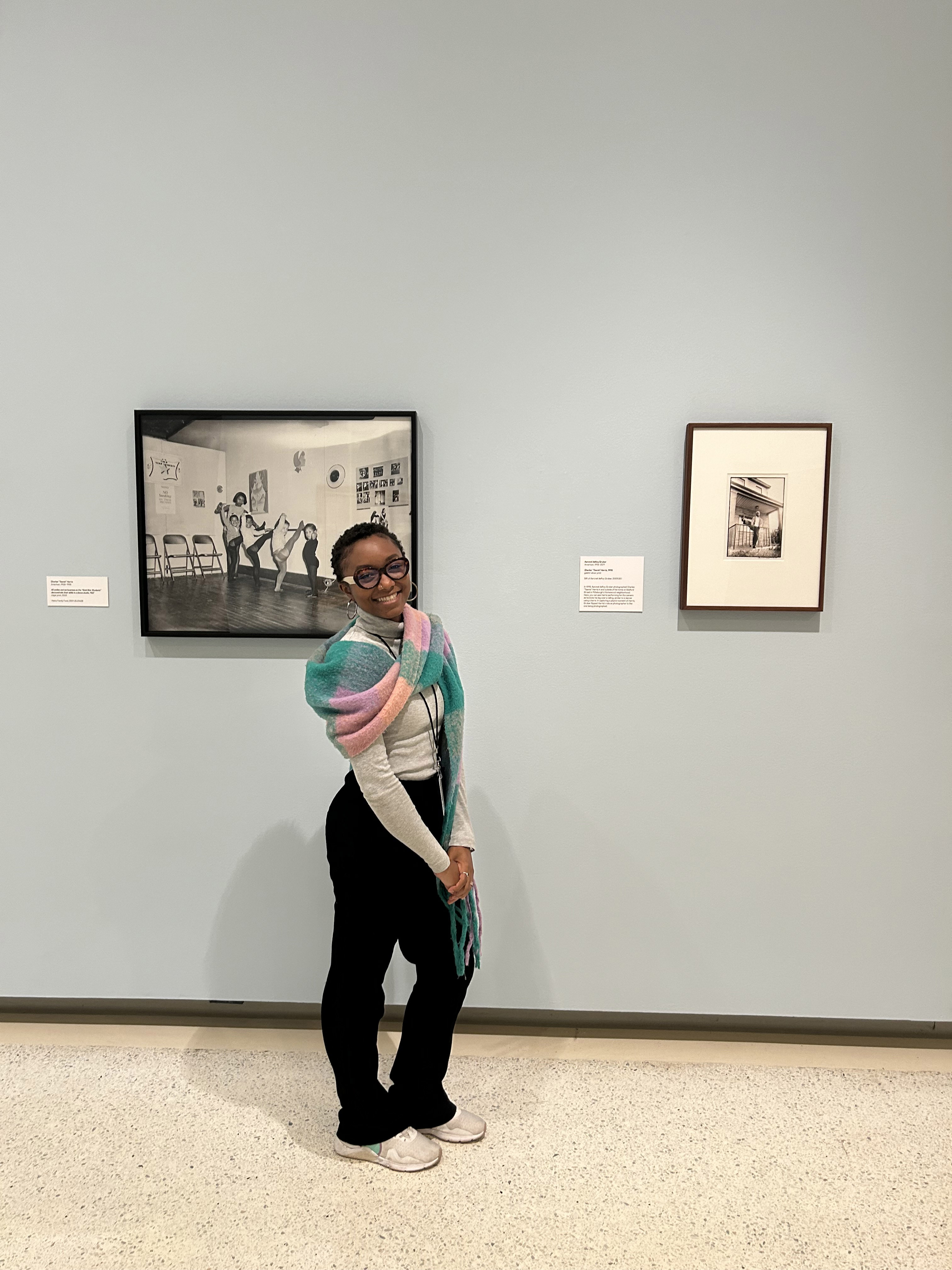 A woman standing in front of a blue gallery wall with two framed works hanging behind